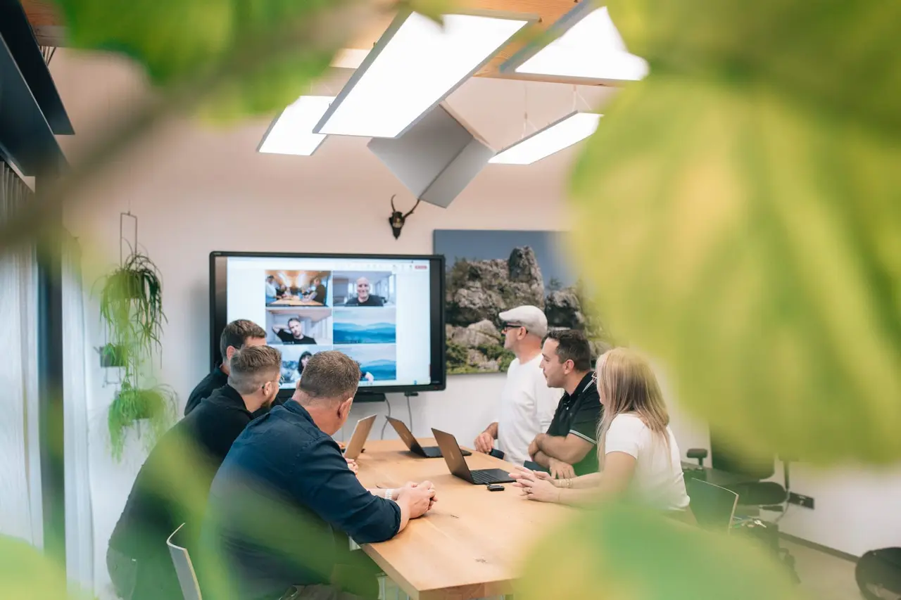 Team von PASSION4IT in einem Meetingraum mit Kunden im Video-Call