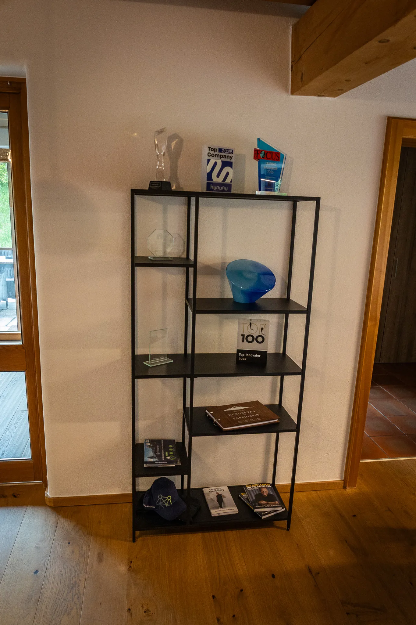 Award shelf in the PASSION4IT office: trophies, innovator awards, kununu Top Company plaque and FOCUS certificate on a steel rack against a light wall.